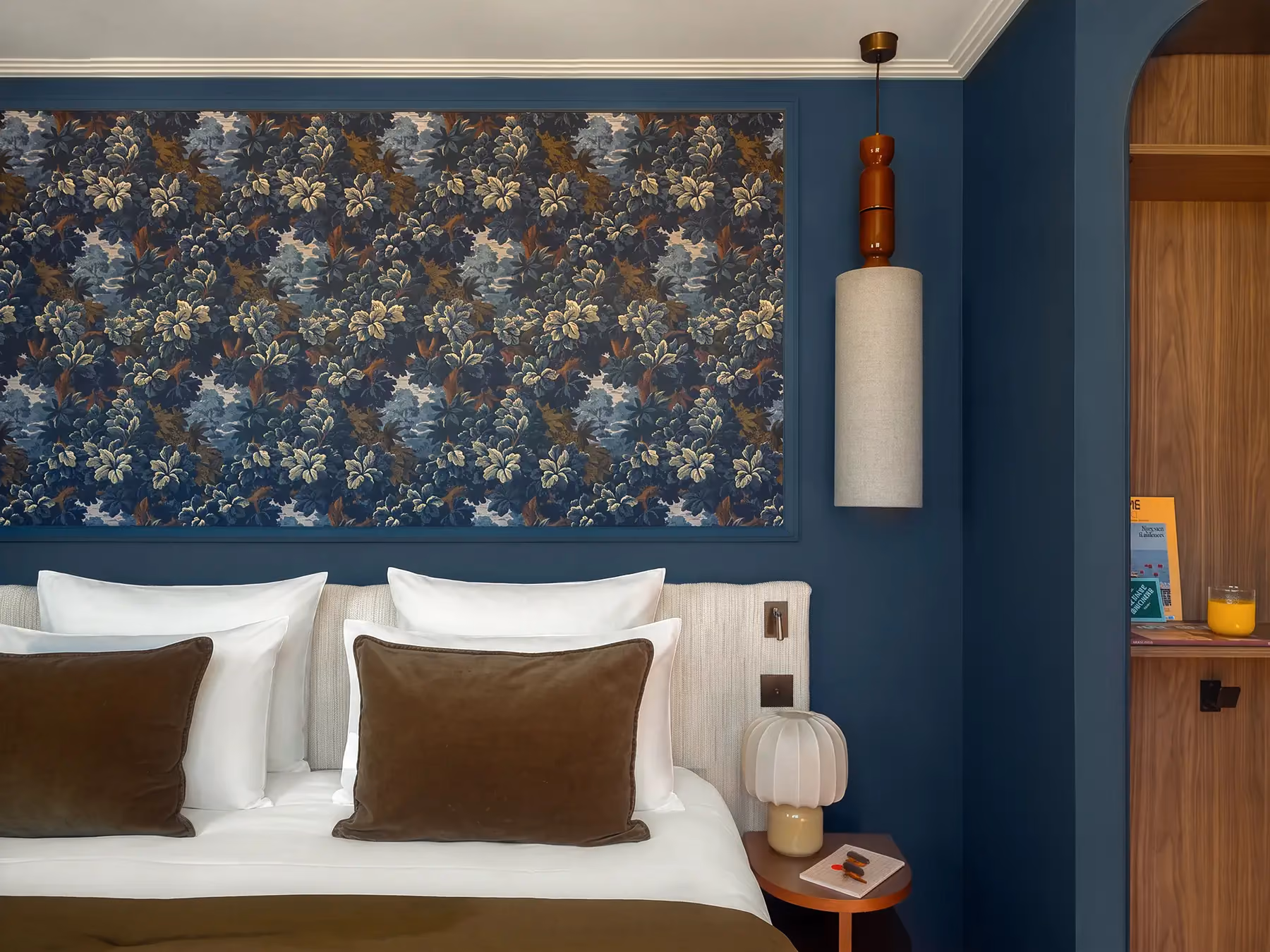 Tête de lit bleu marine avec tapisserie fleurie et coussins marron.