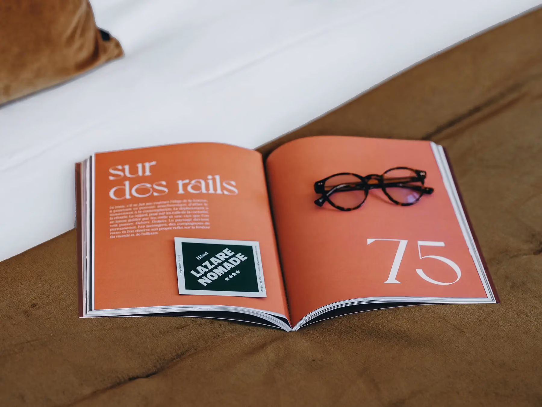 Magazine ouvert sur une page orange "sur des rails" avec des lunettes posées dessus.