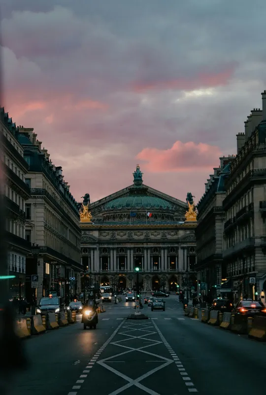Vue de l'Opéra Garnier au bout d'une avenue parisienne, sous un ciel de crépuscule rosé.