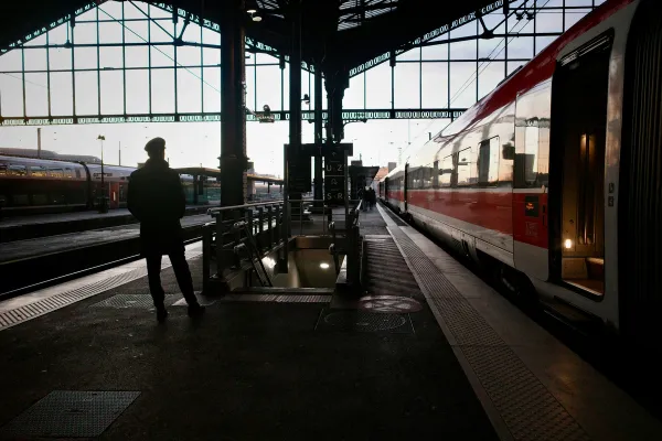 Silhouette d'un homme sur un quai de gare, face à un train à quai sous une verrière métallique.