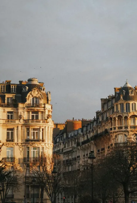 Immeubles haussmanniens parisiens baignés de lumière dorée sous un ciel gris.