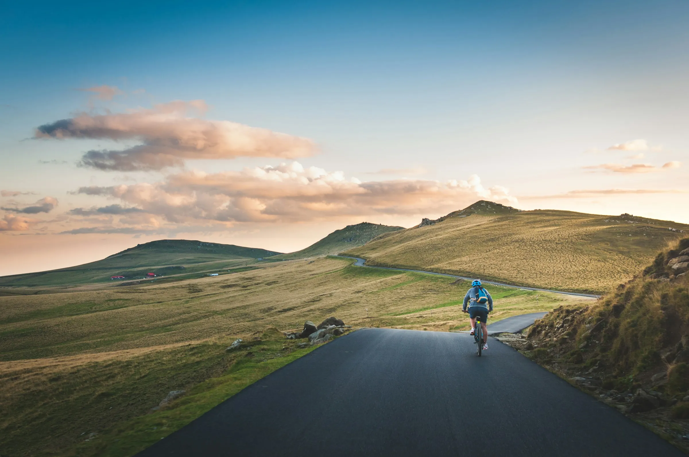 A lone cyclist riding a quiet open road toward rolling green hills at sunrise