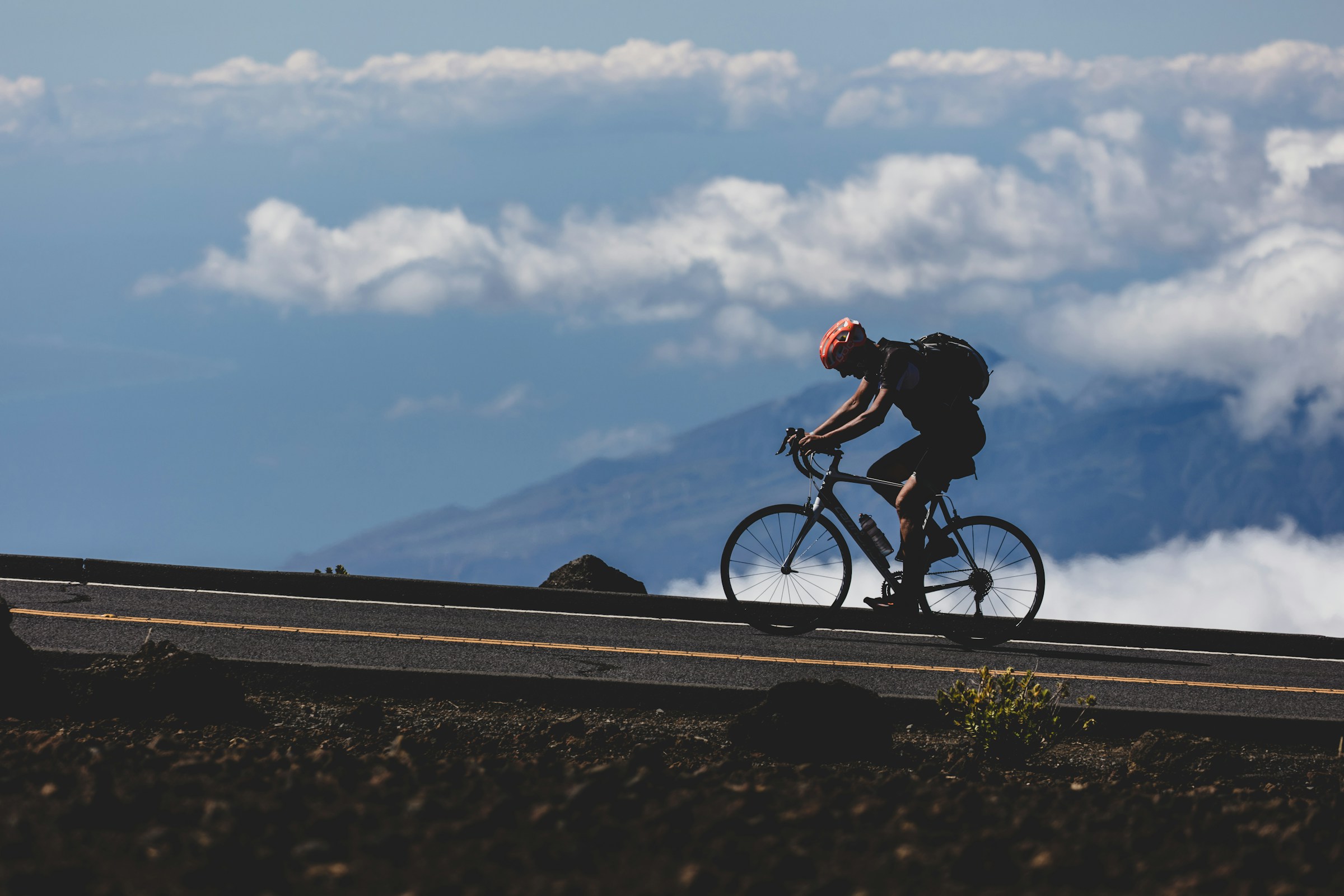 A cyclist climbing a winding road toward a high mountain summit