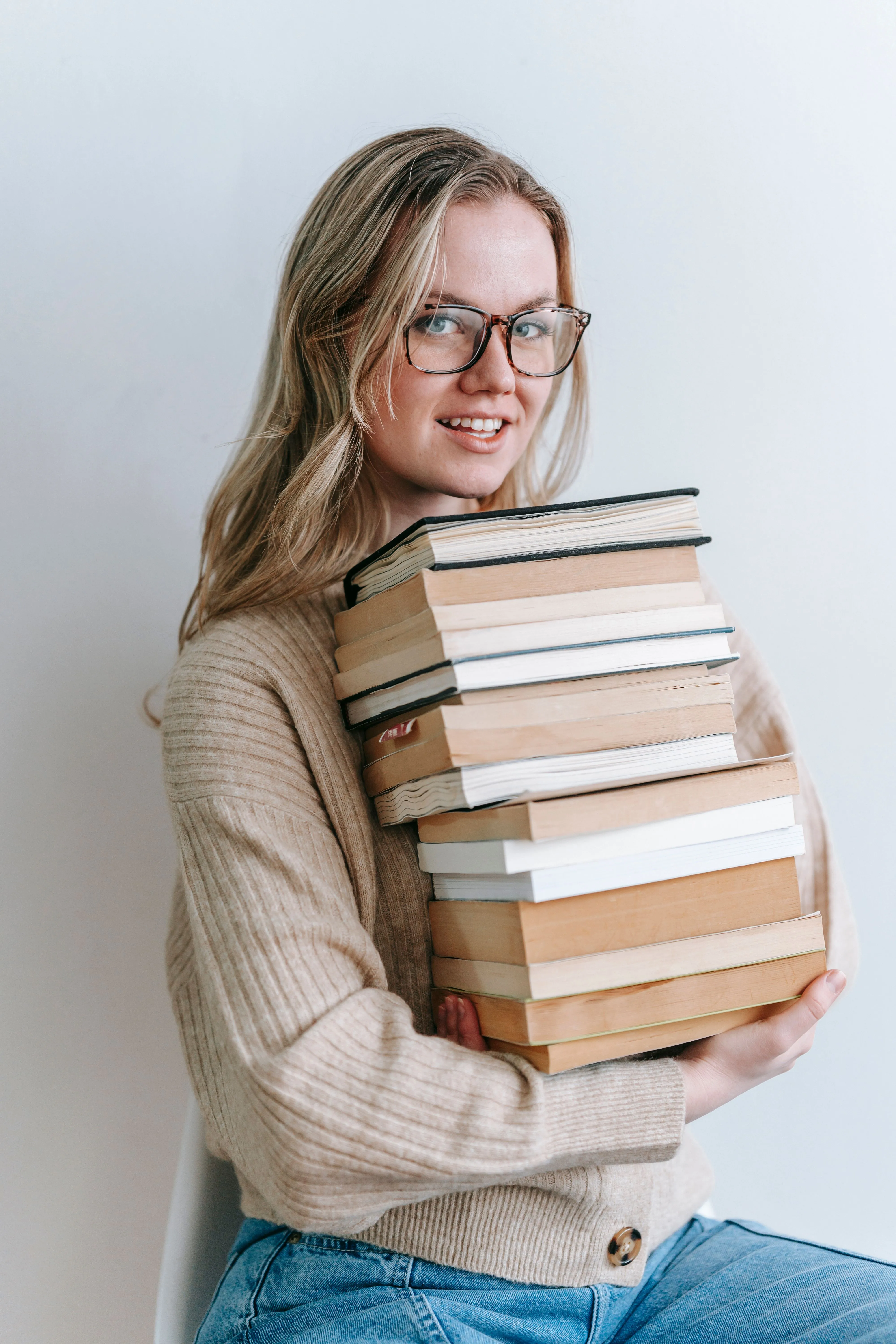 A smiling student in glasses holding a stack of books