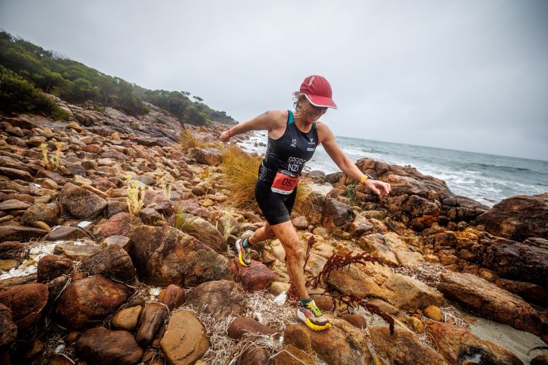 Rebecca running across a rocky stretch of coastline in an Xterra triathlon
