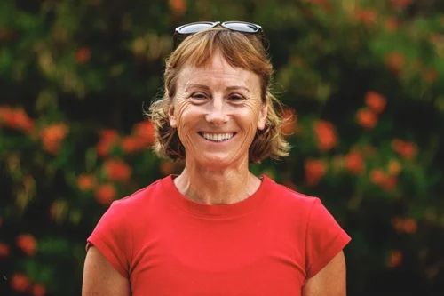Rebecca in a red tshirt against smiling against a background of red flowers.
