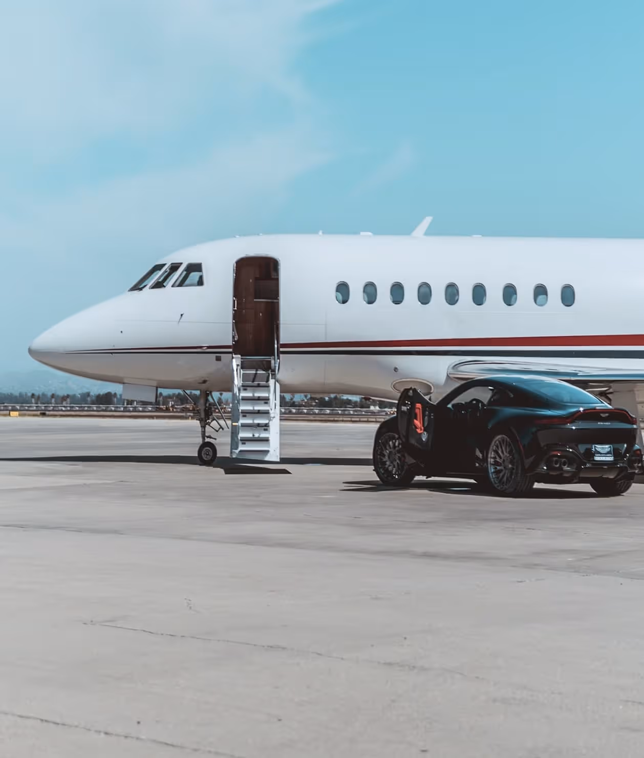 Private jet with stairs down and a black sports car with its door open beside it on a runway.