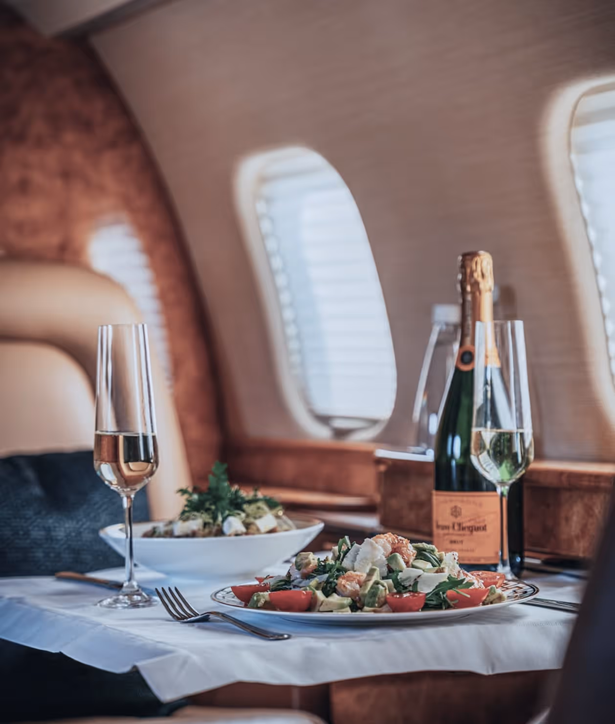 Gourmet salad plates and Veuve Clicquot champagne with glasses inside a private jet.