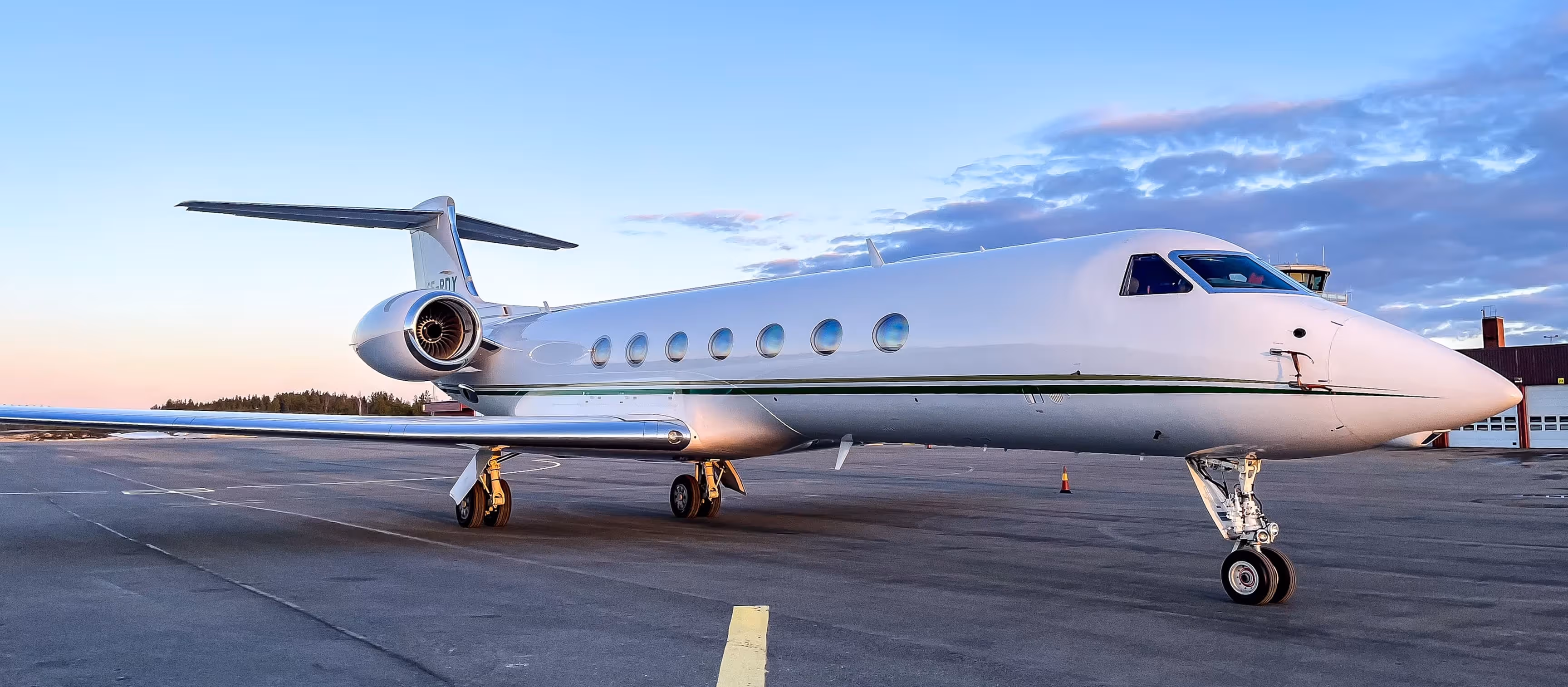 White private jet parked on runway at sunset with a partially cloudy sky background.
