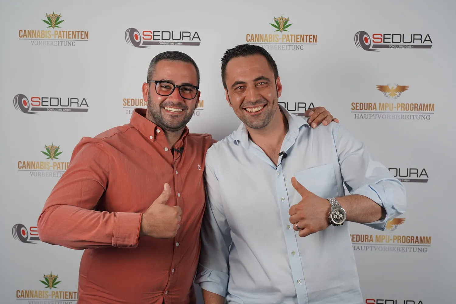 Zwei lächelnde Männer mit Daumen hoch vor einer Wand mit Cannabis-Patienten- und Sedura-Logos.
