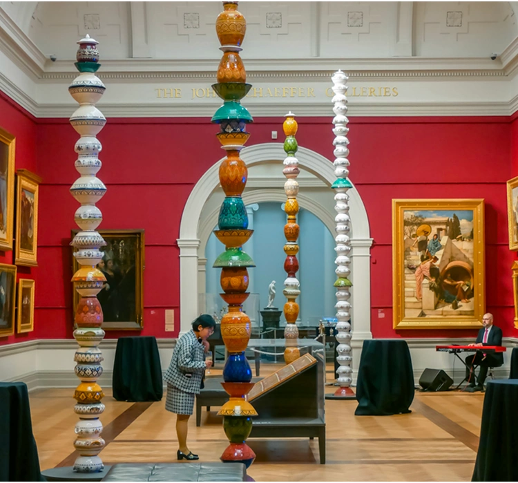 Visitor examining colorful ceramic totem poles in an art gallery with red walls and framed paintings.