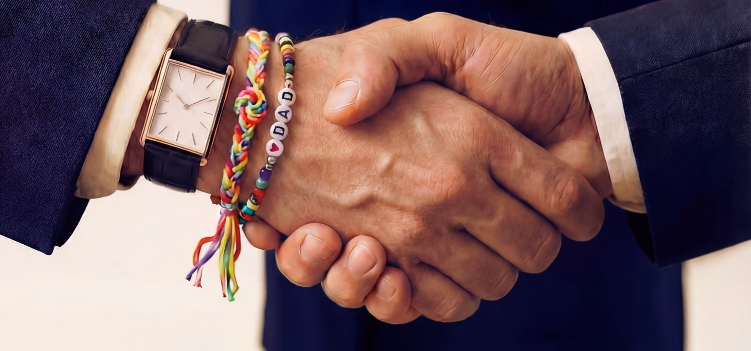 Close-up of two hands shaking, one wearing a wristwatch and colorful bracelets including one spelling 