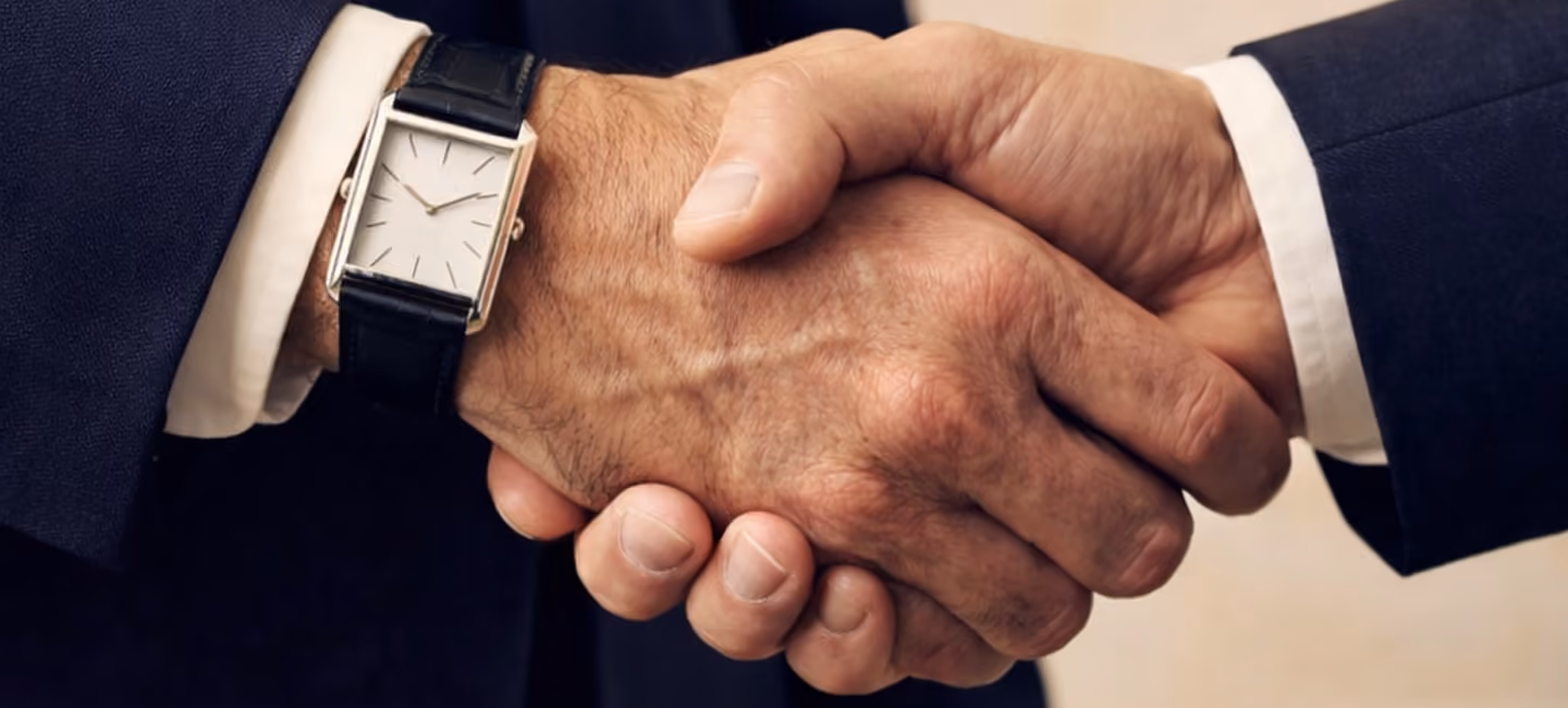 Two men in suits shaking hands, one wearing a classic watch, symbolizing a successful business agreement or partnership