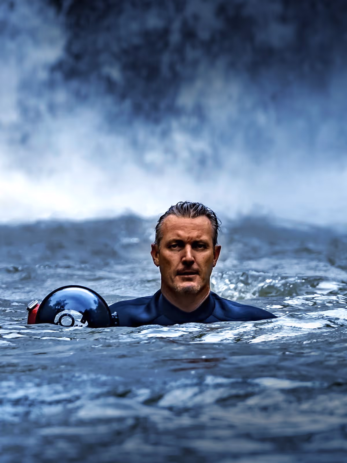 Man in a wetsuit swimming in water, holding a black and red underwater camera housing.