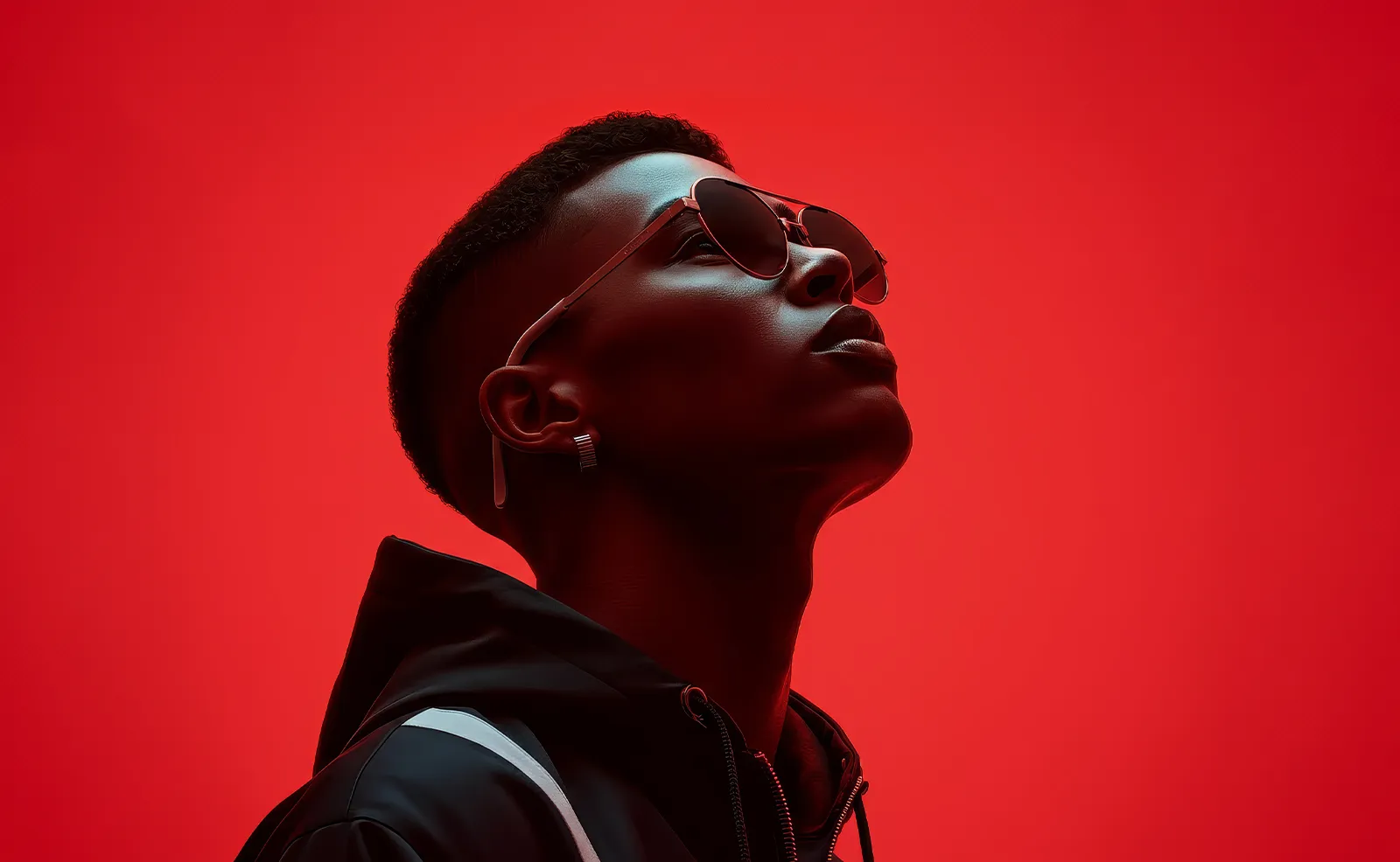 Confident young man wearing sunglasses and a black jacket against a bold red background.