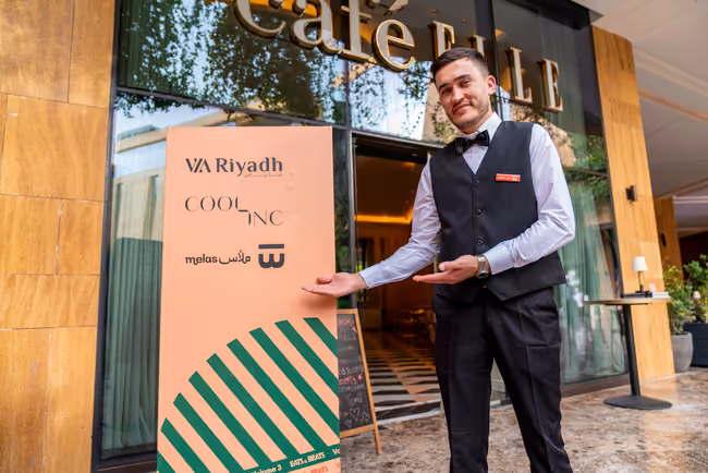 Melas waiter carrying a tray of drinks through a garden lit for an evening festival