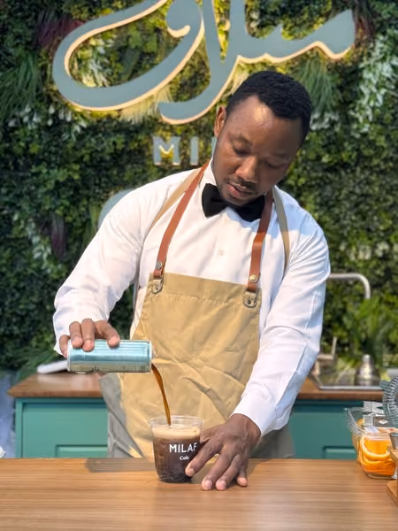 Café server in uniform pouring from a silver pot at a marble table