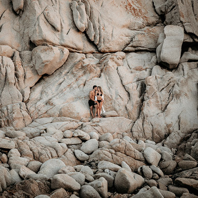 Ein verliebtes Paar steht für ein Couple Shooting vor einer Felswand am Strand von Sardinien.