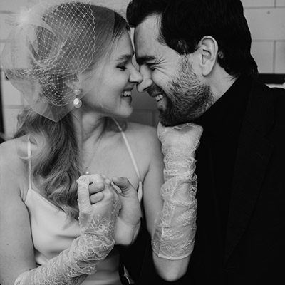 Nahaufnahme eines Hochzeitspaares in einem Pariser Café, das sich lachend gegenüber sitzt und Händchen hält.