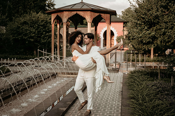 Wedding Shooting in Marokko. Der Bräutigam trägt seine Braut durch einen Garten mit Pavillon.