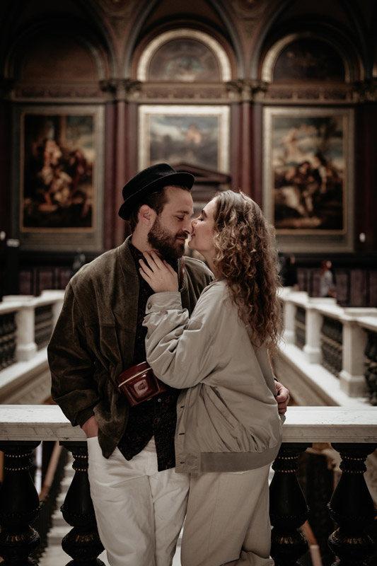 Ein lässig gekleidetes Paar steht in einer Kunstgalerie und schaut sich im Rahmen eines Couple Shootings verliebt an.