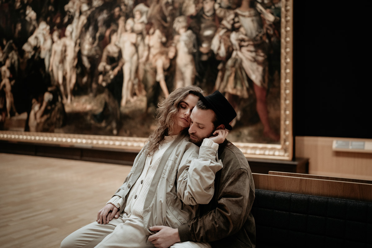 Während eines Fotoshootings in einer Kunsthalle, sitzt eine Frau bei ihrem Freund auf dem Schoß.
