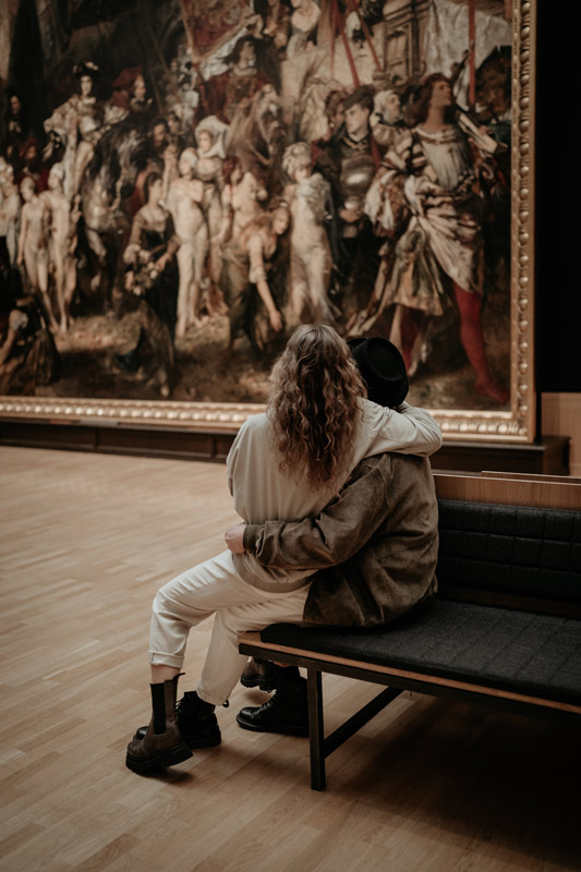 Ein Pärchen sitzt auf einer Bank und schaut ein Gemälde in einem Museum an. Paar-Shooting.
