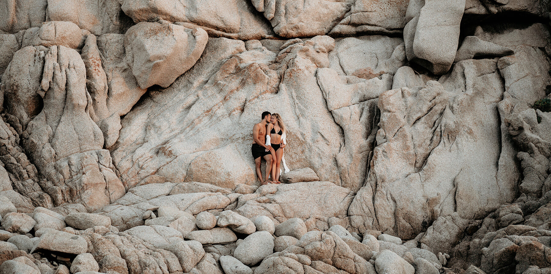 Ein verliebtes Paar steht für ein Couple Shooting vor einer Felswand am Strand von Sardinien.