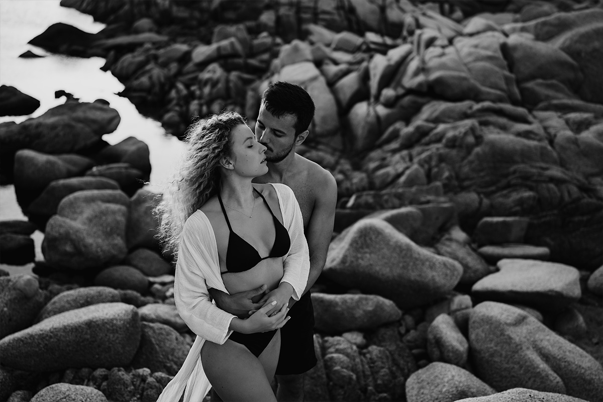 Ein Pärchen steht im Rahmen eines Fotoshootings am felsigen Strand von Sardinien.