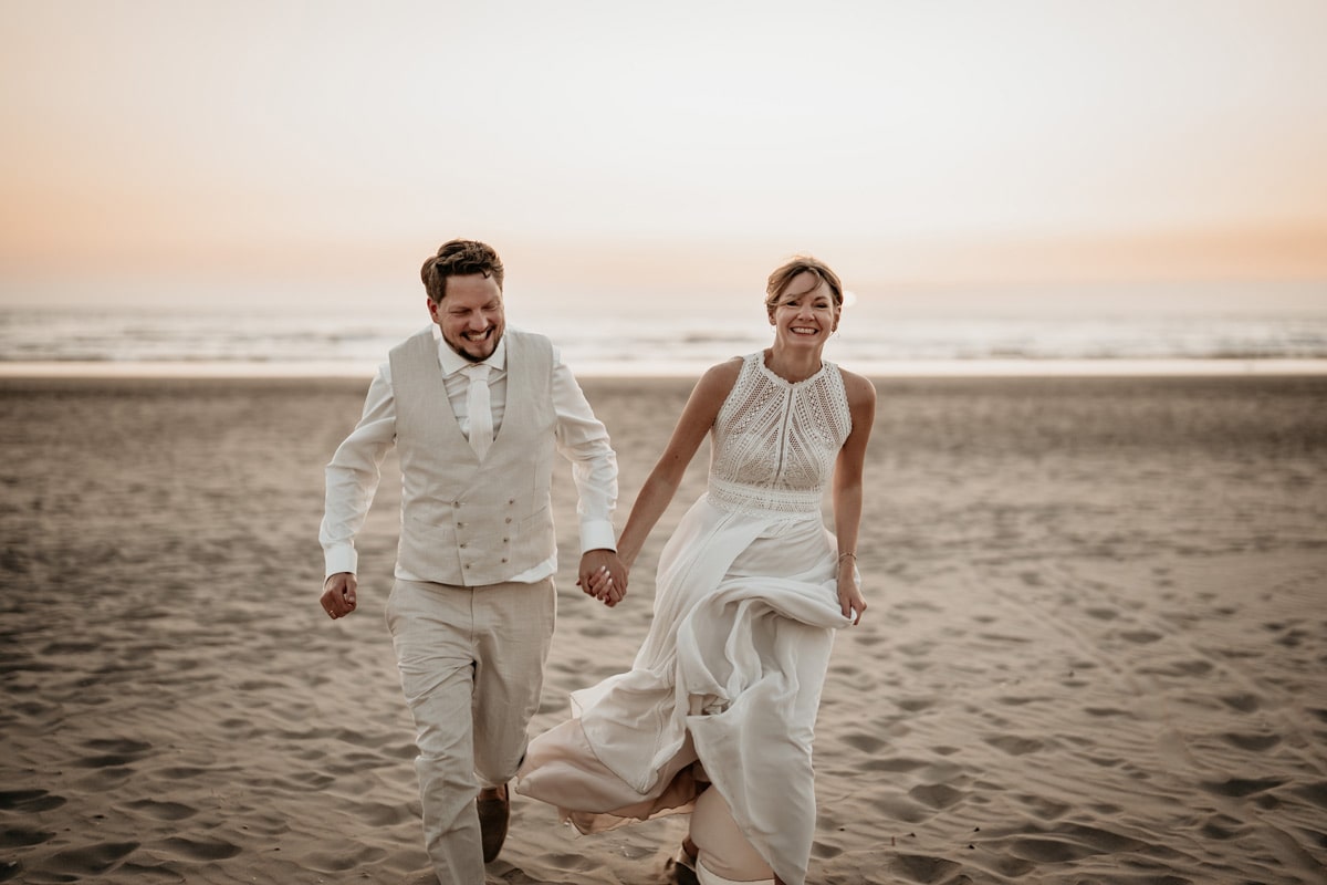 Hochzeits-Shooting am Strand. Das Brautpaar läuft händchenhaltend am Strand von Zandvoort entlang.