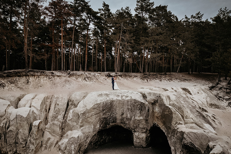 Ein Brautpaar steht in einem Sandsteingebirge mit Kiefernwäldern im Hintergrund.