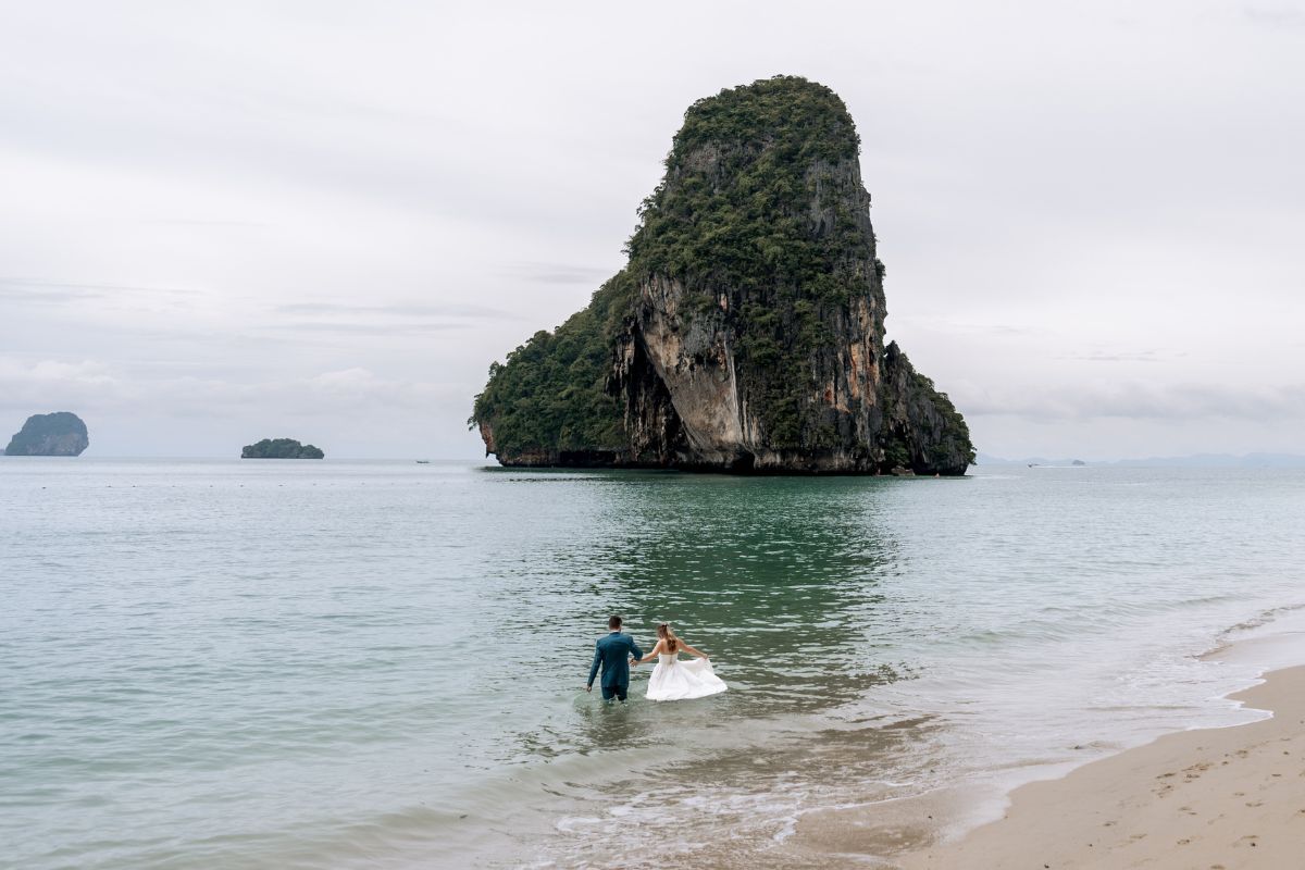 wedding couple walks into ocean in full wedding attire at krabi beach thailand