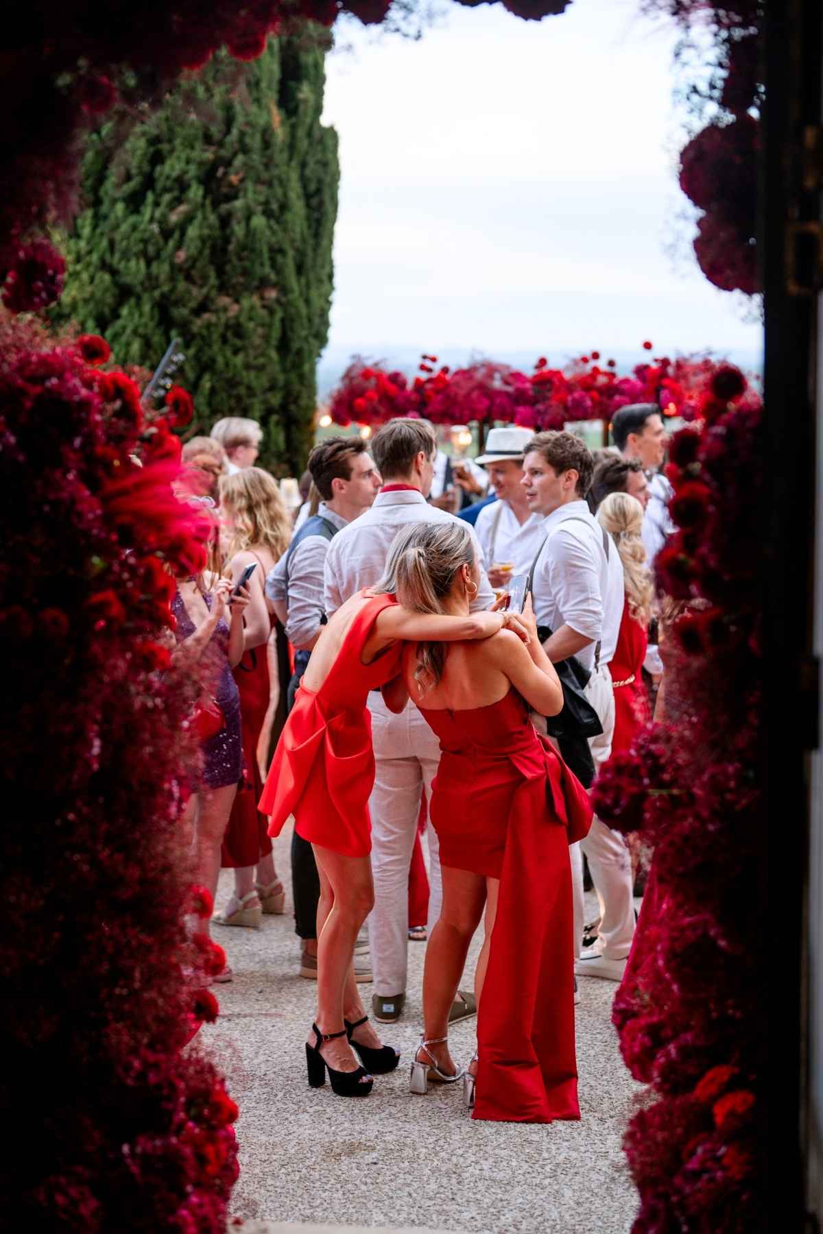 Stylish wedding guests celebrating beneath dramatic red floral installations in Italy