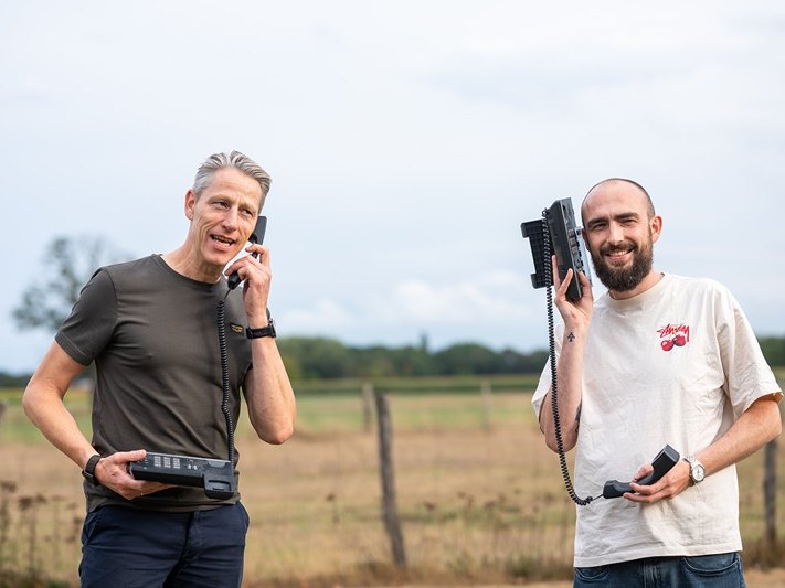 Two Telsmart colleagues in a field, one holding a corded desk phone