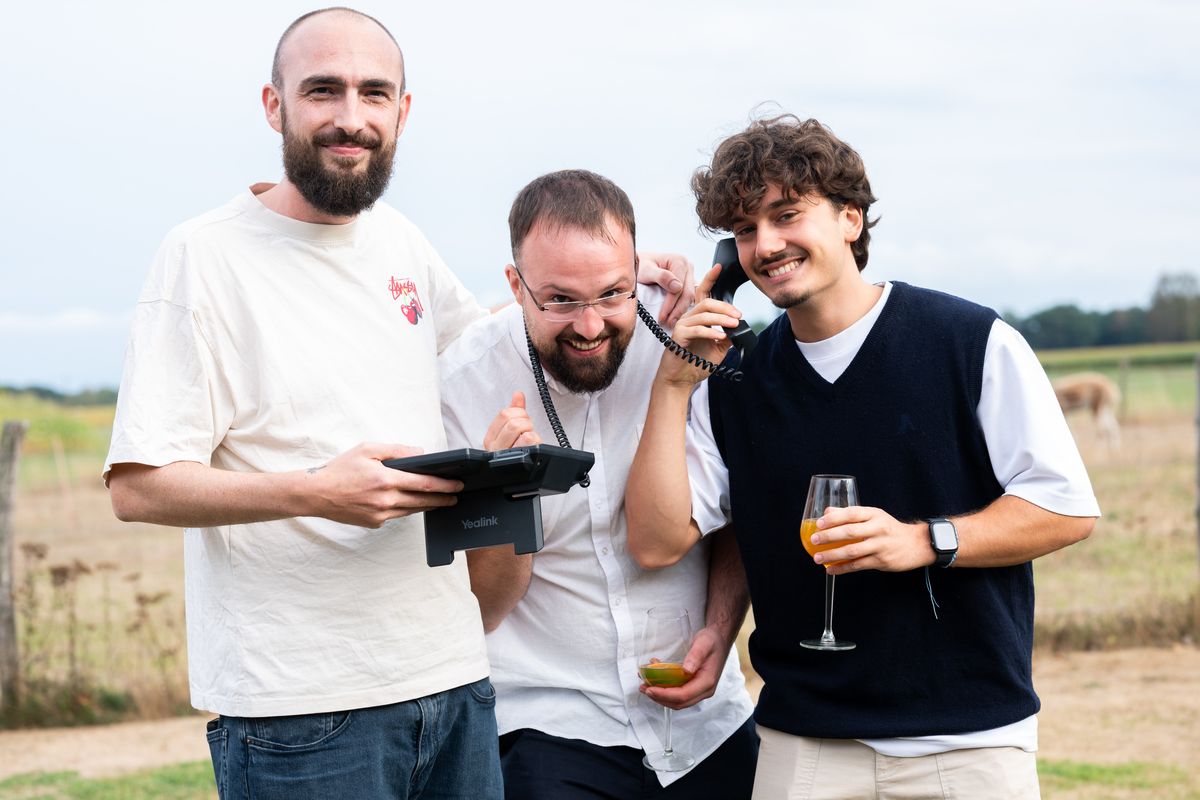 Three Telsmart colleagues outdoors, one holding an old corded telephone to his ear