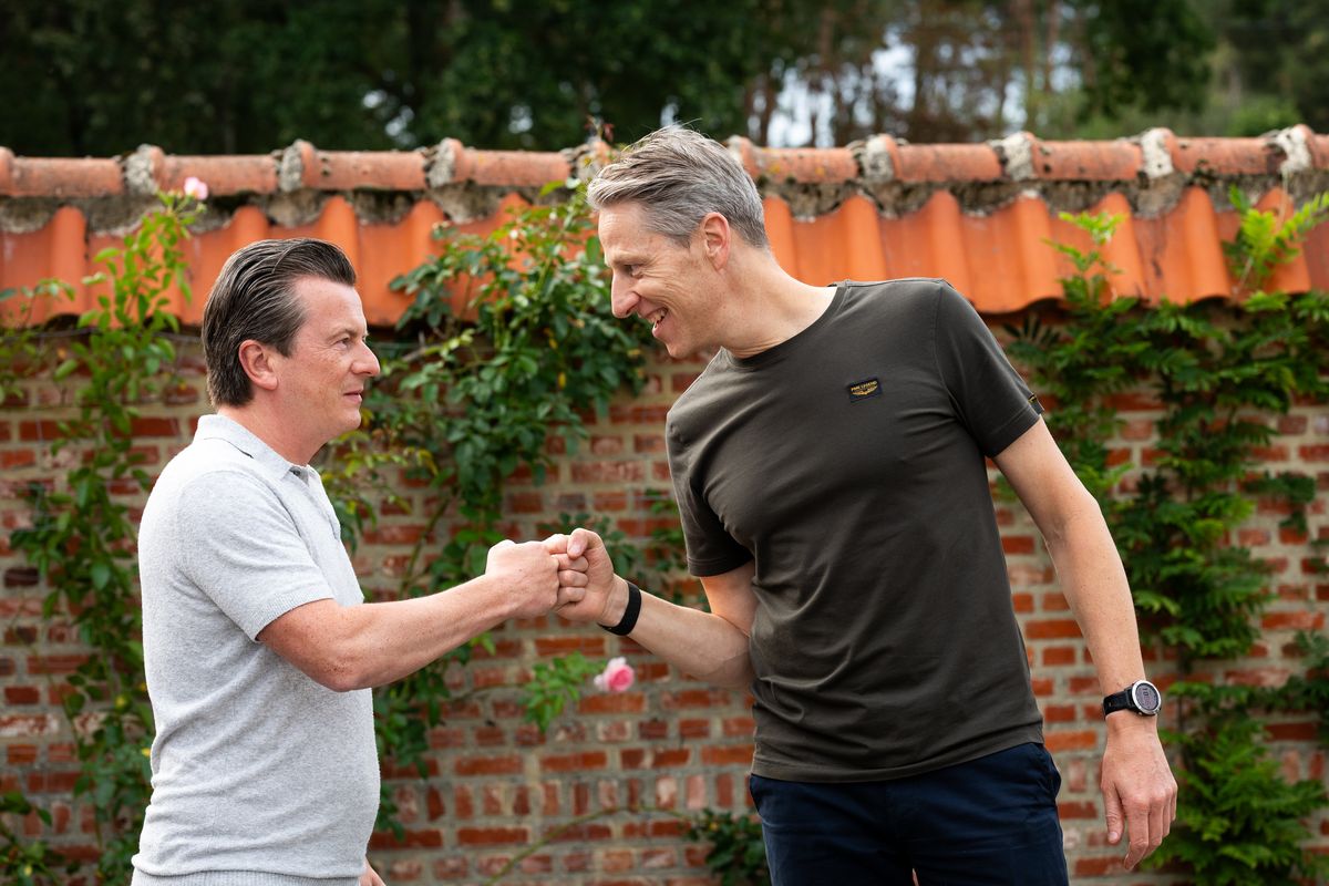 Two Telsmart colleagues bumping fists in front of a brick wall covered in flowers