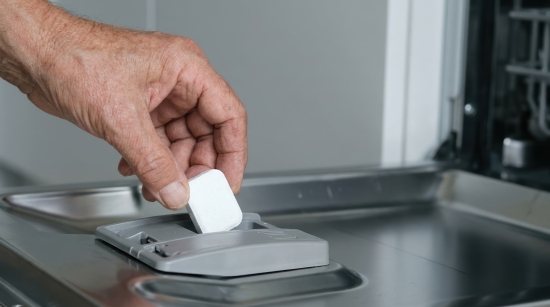 Hand placing a dishwasher tablet into the detergent compartment of a modern dishwasher, representing everyday domestic appliances.