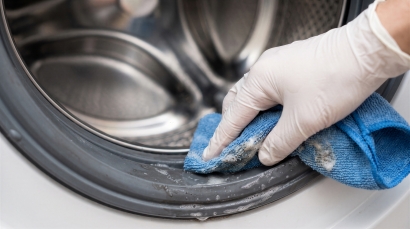 Person cleaning a washing machine door seal with a cloth to help maintain the appliance and prevent the need for washing machine repairs.