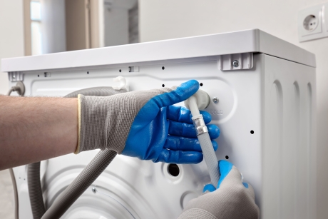 Washing machine engineer wearing gloves repairing connections at the back of a washer to help prevent appliance faults.