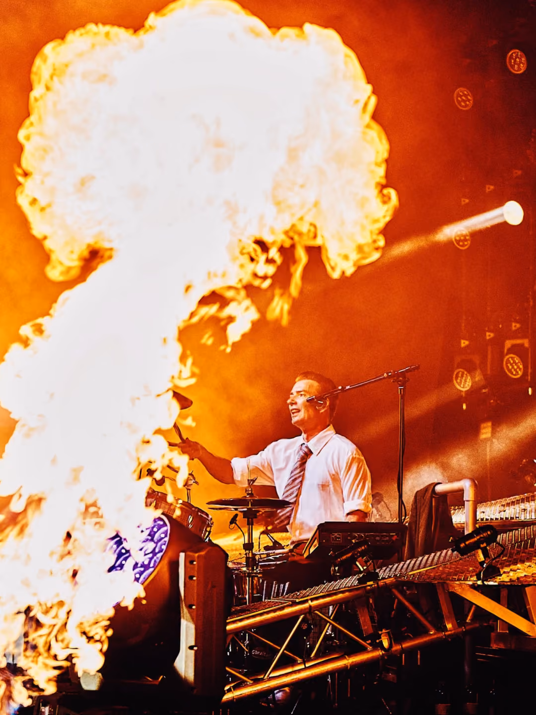Laust Sonne playing drums among large flames on stage.