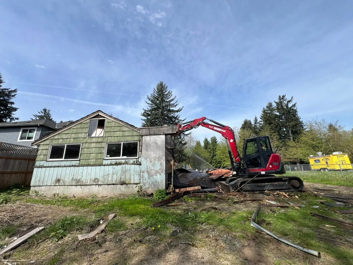 A contractor operating an excavator for demolishing a wooden home in Seattle