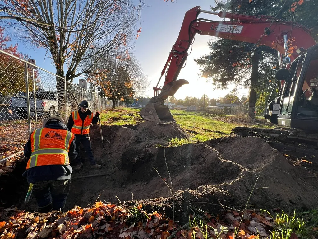 Two contractors in an excavated lot with an excavator beside them in a grassy lot in Seattle