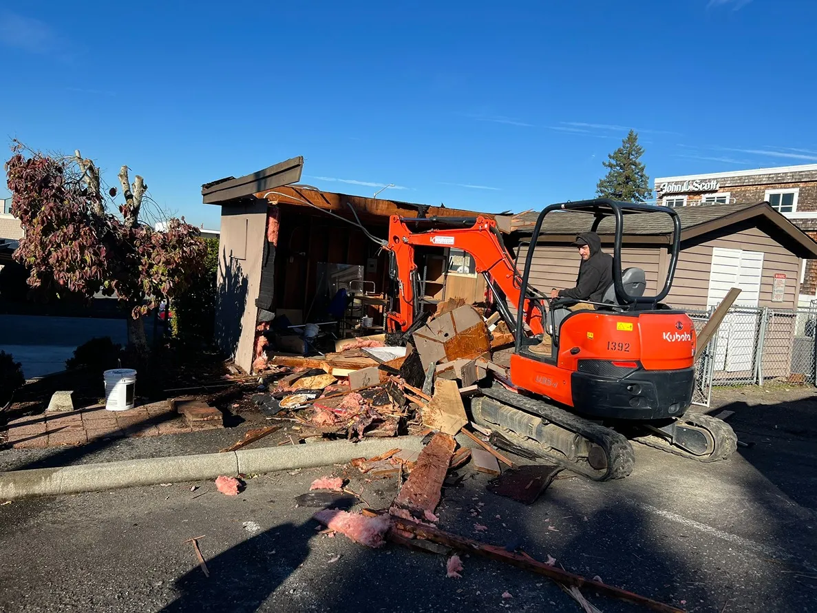 A contractor operating a mini excavator for demolishing a wooden shed