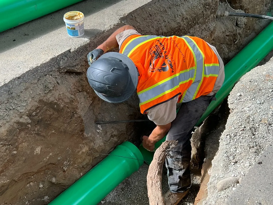 Contractor installing a green sewer pipe in an open trench in a Seattle residential area