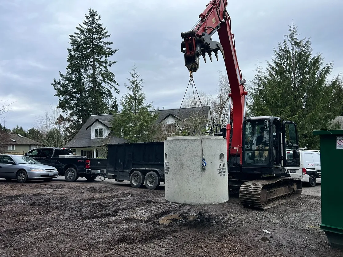 An excavator holding a sewer manhole yet to be installed in a Seattle residence