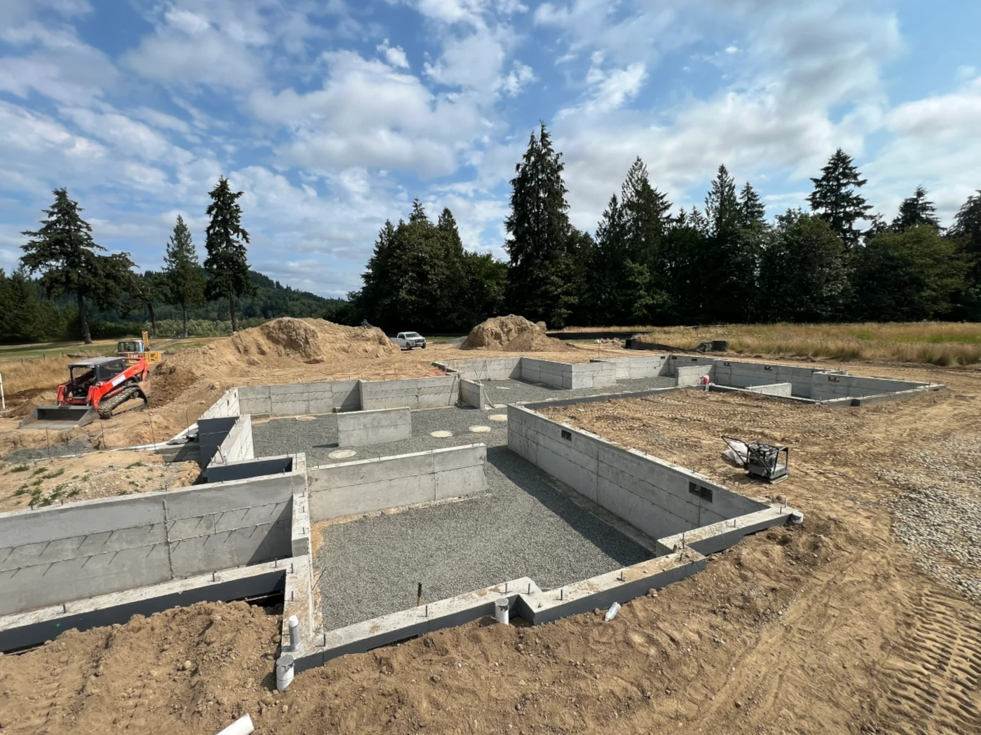 Completed crawlspace foundation walls with compacted gravel base and pier pads on a cleared building site