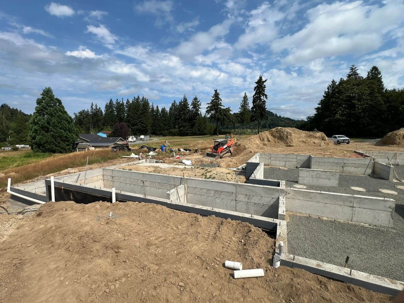 Compact track loader backfilling around a newly poured crawlspace foundation on a residential lot
