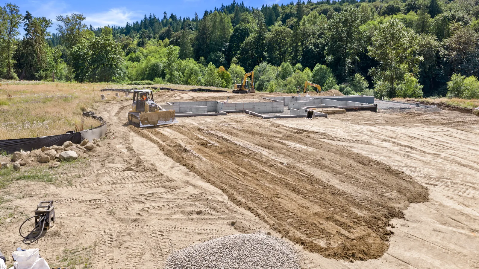 	Lineup of excavation equipment — vibratory roller, two mini excavators, dozer, and compact track loader — with crew members alongside