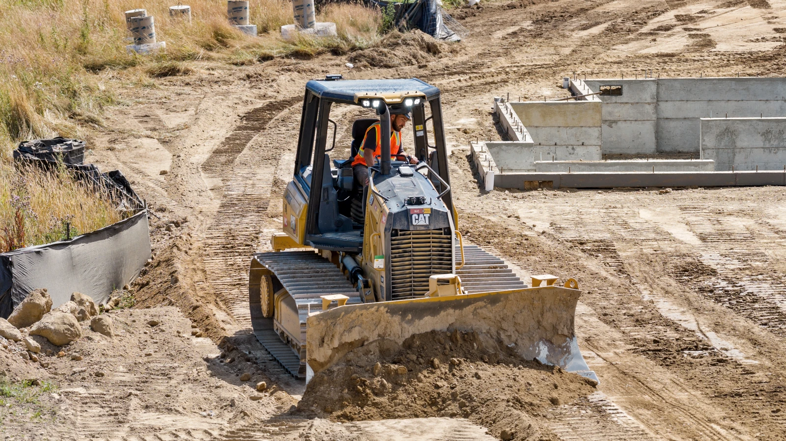 Mighty Arm Excavation operator grading a building pad with a CAT track dozer beside poured concrete foundations