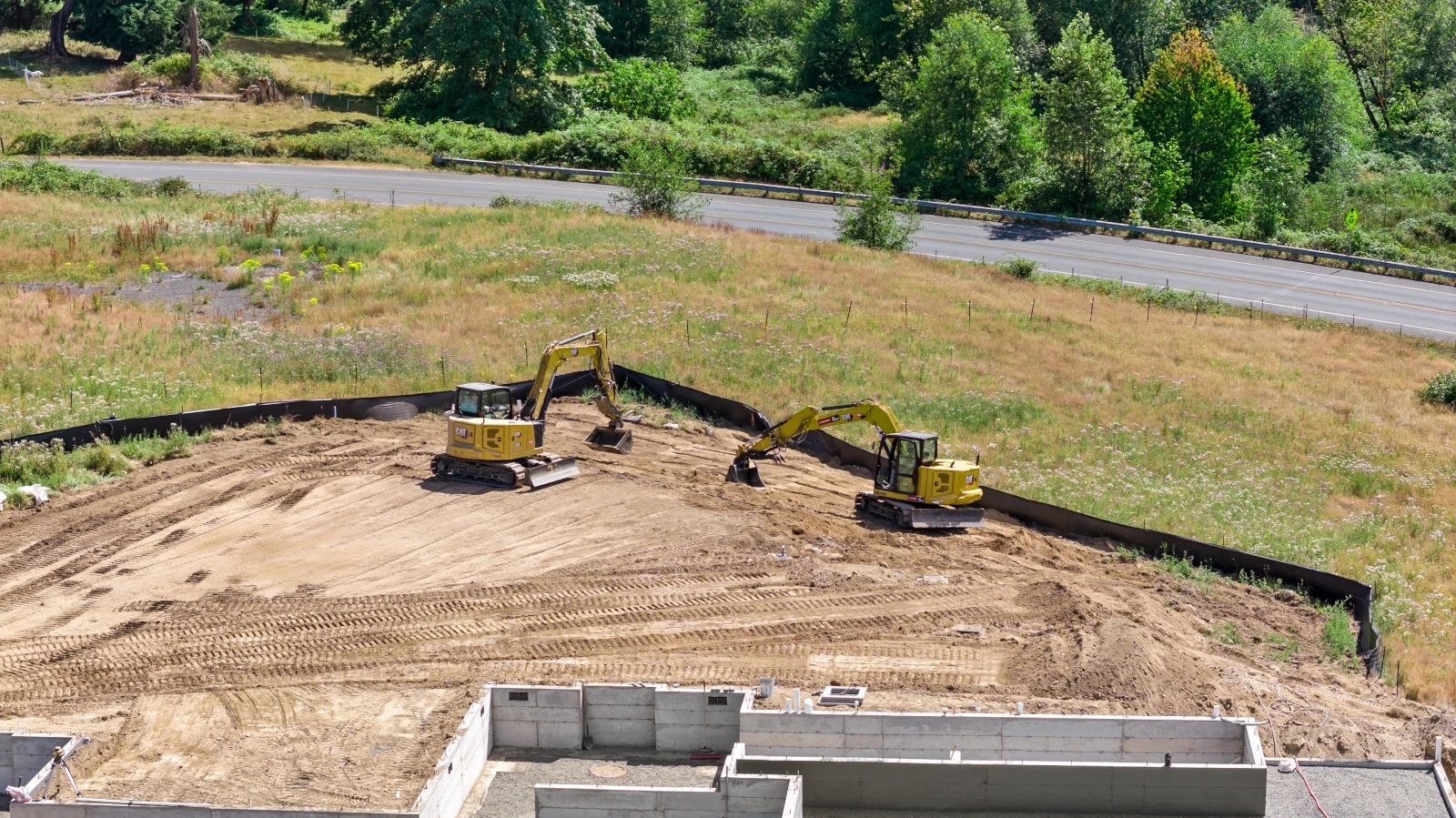 Two CAT compact excavators cutting and grading a residential building pad inside a silt fence perimeter